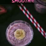 An overhead shot of strawberry banana smoothie garnished with chopped banana in two glass containers and placed on a wooden bowl. There are two red and white straws on the side.
