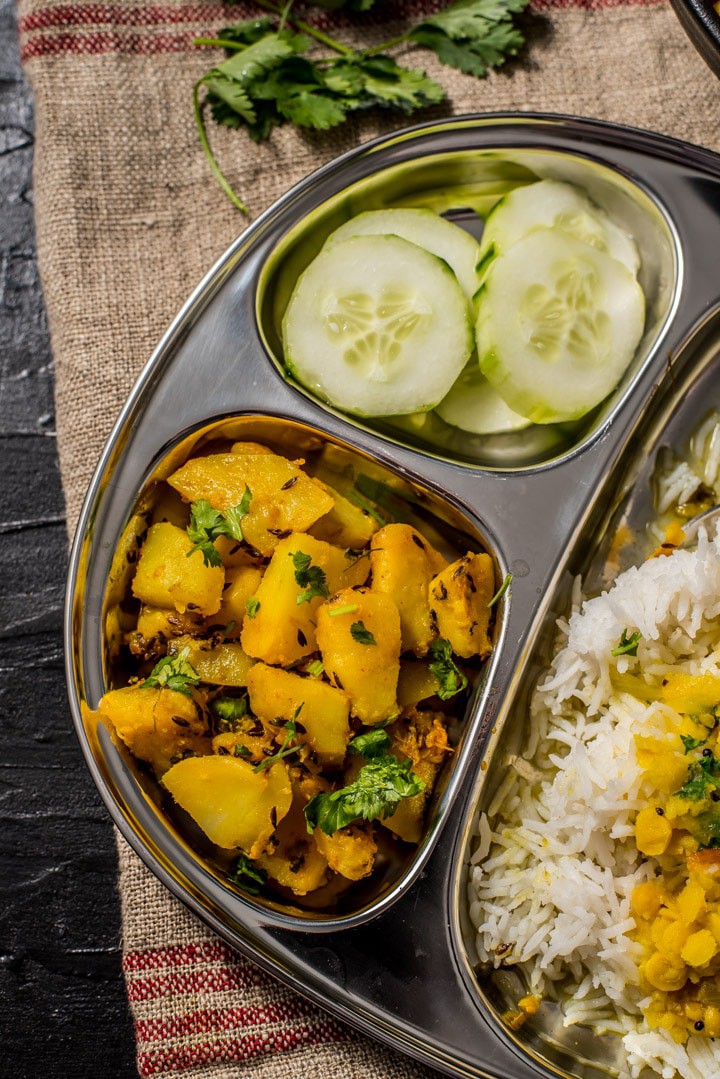 Jeera aloo served with dal and rice and cut cucumber slices