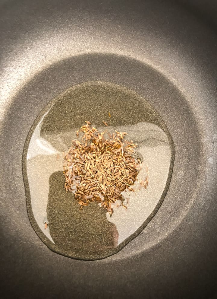 A tempering of cumin seeds in a non-stick wok