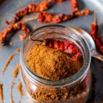 An overhead shot of Rasam powder in a glass bottle with a whole dried red chili on top