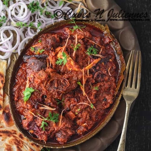 An overhead shot of Bhuna gosht served with onions and naan