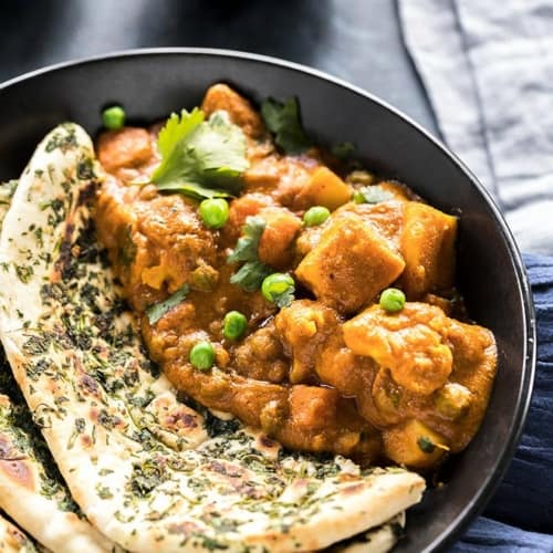 Vegetable Korma served with naan in a black bowl