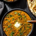 An overhead shot of Dal Makhani recipe served with a sliver of butter and accompanied with garlic naan and aloo gobi