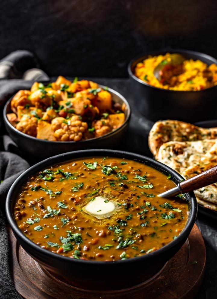 Dal Makhani served in a black bowl accompanied with aloo gobi and garlic naan