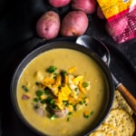 Potato corn chowder soup served in a black bowl with crackers along with a few red potatoes on the side