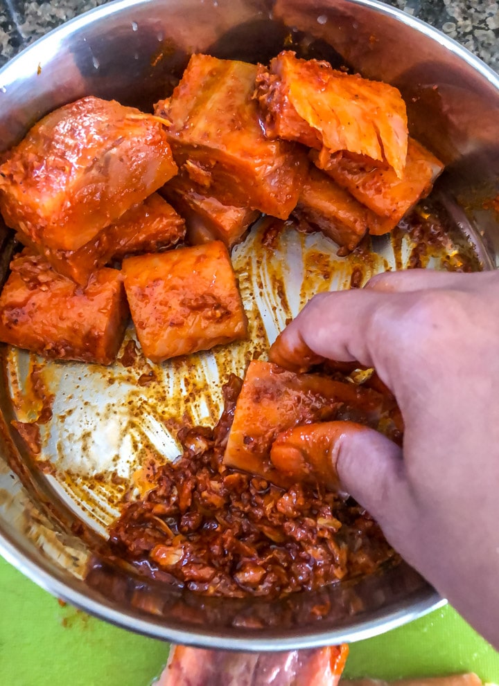 A right hand dipping the square pieces of the salmon into the salmon tikka marinade coating it on both sides.