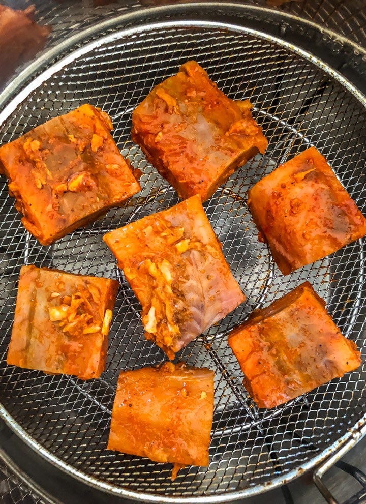 7 pieces of tandoori salmon cut into squares, resting on the greased Mealthy CrispLid tray. They are arranged in a circle with one piece in the middle and 6 around the edges.