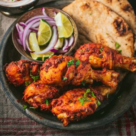Tandoori chicken served with naan and sliced limes and onions