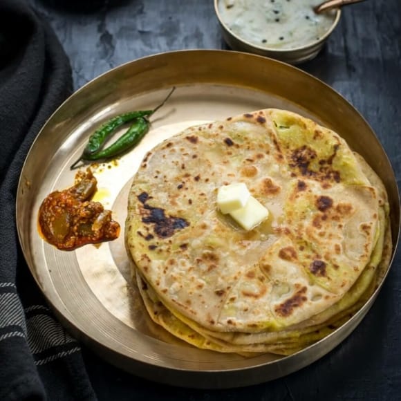 An overhead shot of Aloo paratha served with a dollop of butter, pickles and green chilies