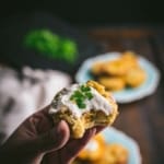 A hand holding a mashed potato muffin topped with sour cream