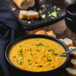 Broccoli Cheddar Soup served in a black bowl accompanied by baguettes