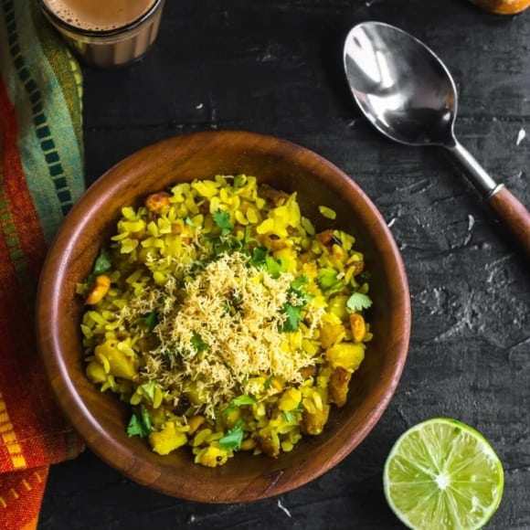 An overhead shot of Batata Poha in a brown bowl with a side of lime