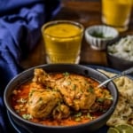 A close up shot of Indian curry chicken served in a gray bowl accompanied with naan and lassi