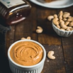 Cashew butter served in a ramekin with cashew pieces and a bottle of honey on the side