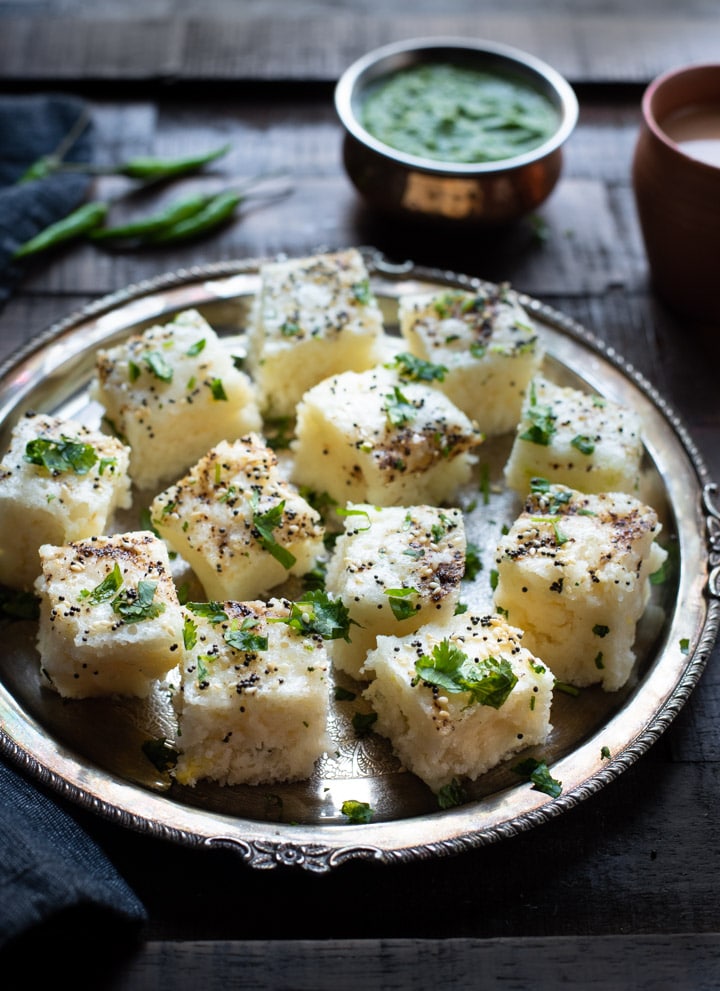 Pieces of Instant Rava dhokla served in a metal plate accompanied by green chutney