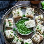 A plate full of sooji dhokla served with green chutney and tea