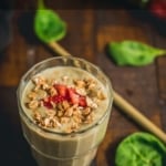 a glass of strawberry banana spinach smoothie garnished with strawberry and granola