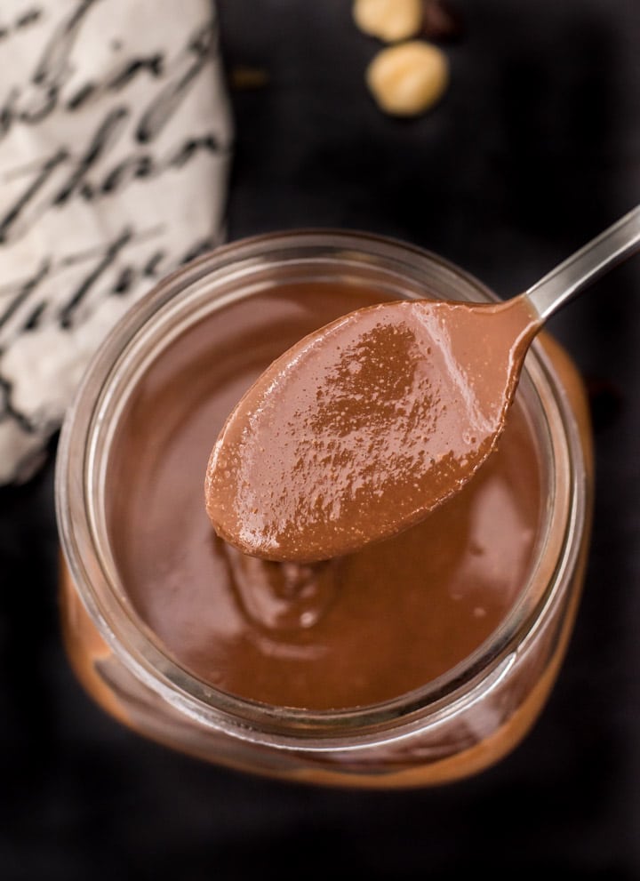A spoonful of hazelnut butter being scooped out of a glass jar