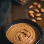 Almond butter in a black bowl with almonds on the side