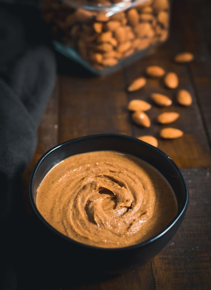 Almond Butter served in a black bowl with almonds placed on the side