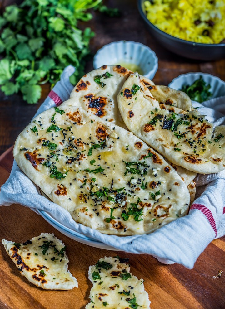 A fresh stack of garlic naan with chopped cilantro on a white dish towel next to a cup of cilantro.