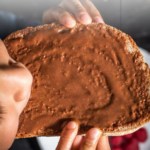 A child eating a toast that is smeared with chocolate hazelnut spread