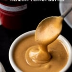 A white bowl of creamy peanut butter with a spoon scooped in the peanut butter and the words Healthy Peanut Butter at the top.