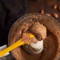 A closeup shot of almond butter scooped in a yellow spatula