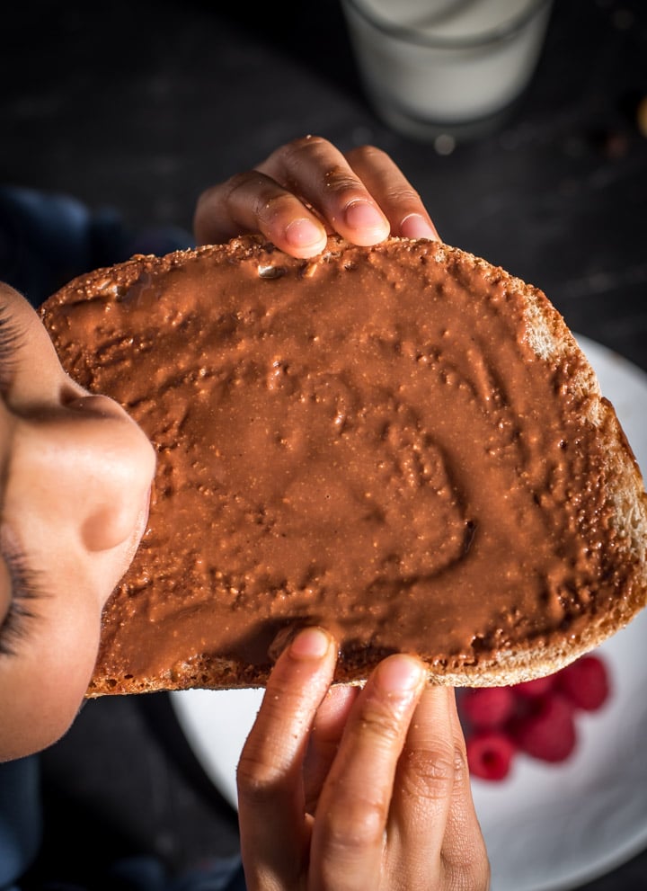 A child eating a toast that is smeared with chocolate hazelnut spread