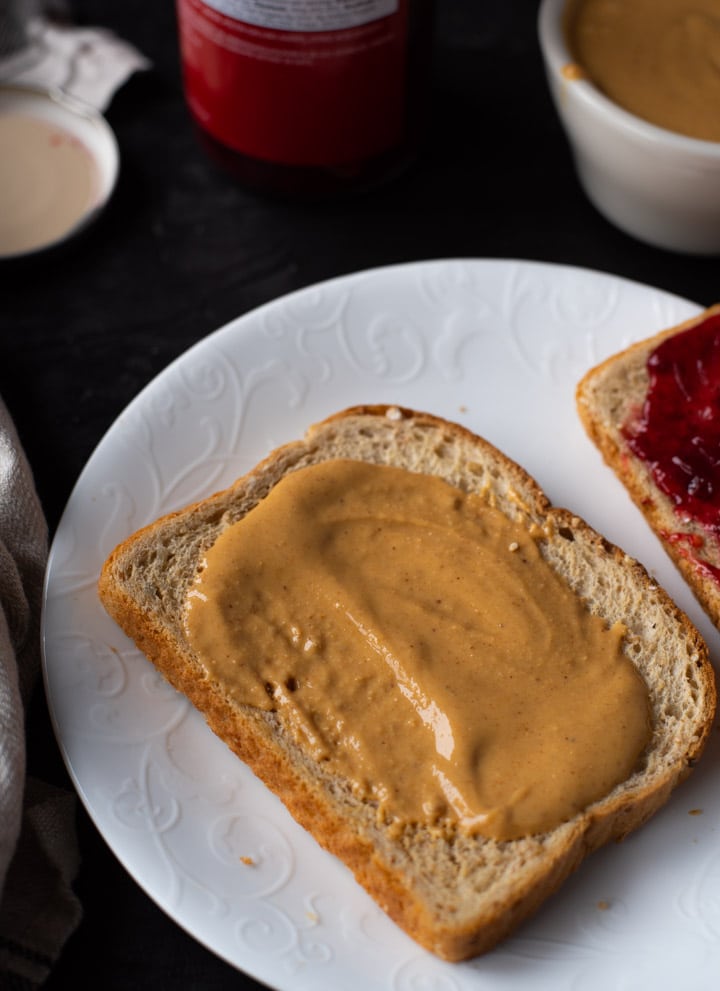 A white plate with a piece of bread with peanut butter and another piece of bread with jelly on it.