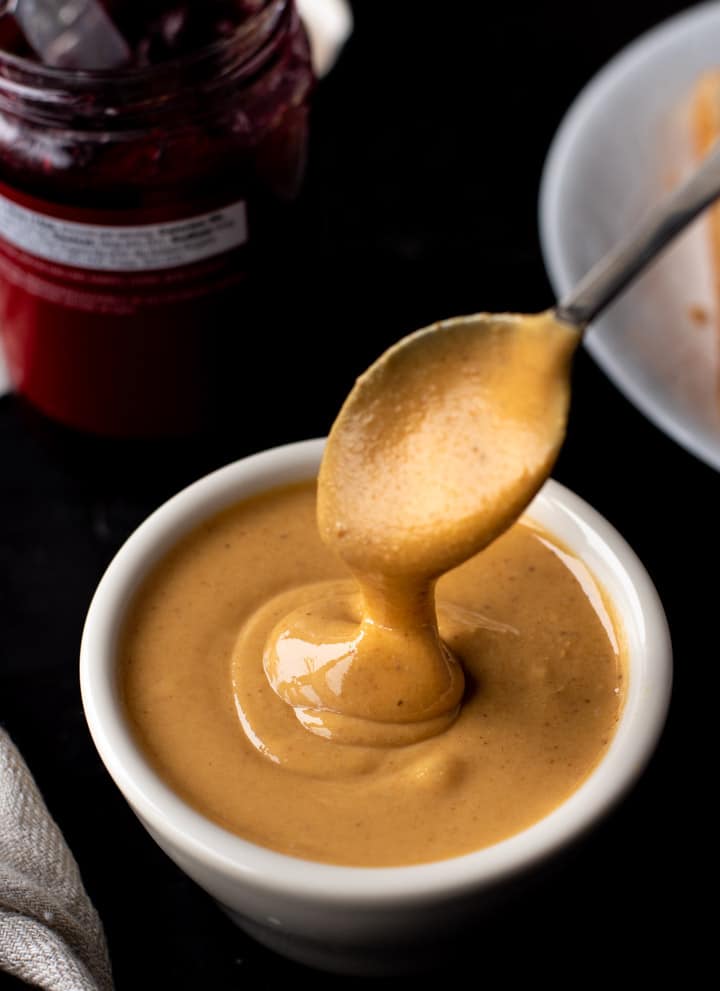 A white bowl of creamy peanut butter with a spoon scooped in the peanut butter.
