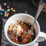 A white coffee mug with a chocolate mug cake inside topped with vanilla chocolate ice cream, sprinkles and chocolate sauce with a fork sticking out of the mug and the words 5 Minute Chocolate Mug Cake Recipe at the top.