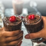 Two hands each holding a glass of chocolate chia pudding