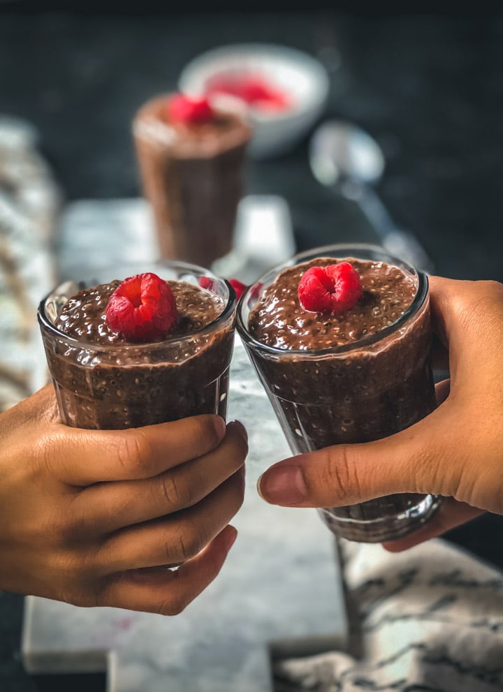 Two hands each holding a glass of chocolate chia pudding