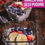 Two glass bowls of vanilla chia pudding topped with banana, strawberry, and blueberry on a wooden table with a spoon in between them and strawberries behind them and the words Delicious Chia Seed Pudding in a pink box at the top.