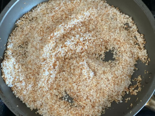 Desiccated coconut along with sesame seeds being roasted in a pan