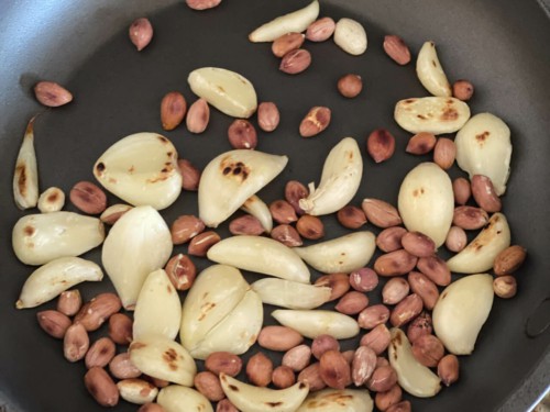 Garlic cloves and peanuts being roasted in a pan