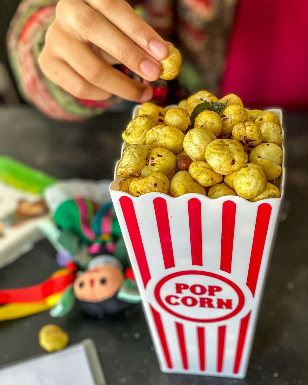 A hand picking a makhana kept in a popcorn box