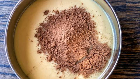 A mixing bowl with condensed milk and cocoa powder on a wooden counter.