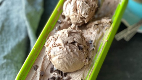 A green tub of double chocolate ice cream with an ice cream scoop and two scoops of ice cream.