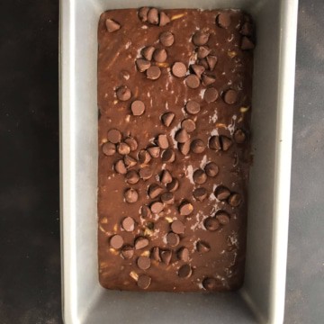 A metal baking dish with chocolate zucchini bread batter topped with chocolate chips before baking.