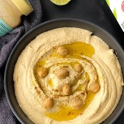 A black bowl of creamy instant pot hummus with olive oil on top and a few extra chickpeas with the words Homemade Hummus Using Instant Pot at the top of the picture.