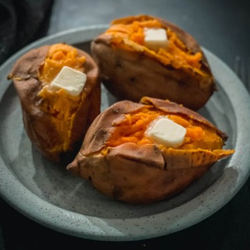 A light blue plate with three baked sweet potatoes with a cut down the middle of each and a pad of butter on top.