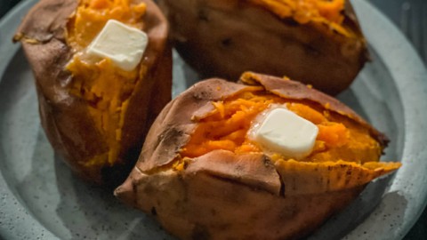 A light blue plate with three baked sweet potatoes with a cut down the middle of each and a pad of butter on top.