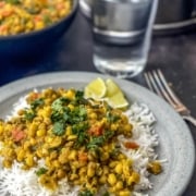 The words 30 Minute in white with the words moong bean curry in yellow below with a picture of moong bean curry on top of rice on a grey plate with a fork to the right and a cup of water in the back.