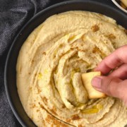 A black bowl of creamy instant pot hummus with a hand dipping a pita chip into the hummus and the words Instant Pot Hummus at the top.