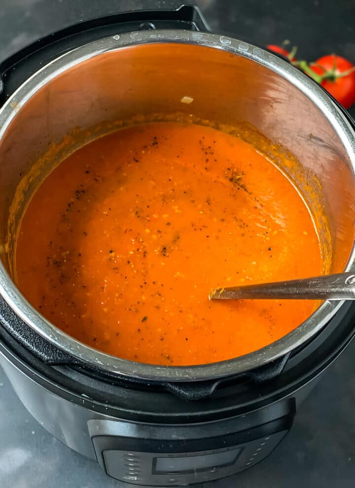An instant pot pressure cooker with a spoon and homemade marinara sauce.