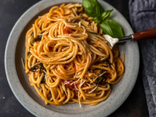 A light grey plate with a serving of instant pot spaghetti with a fork in the right side of the spaghetti pile and some basil at the top.