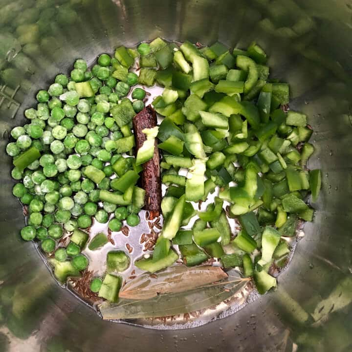 Inner pot with spices, bell pepper, and peas cooking.