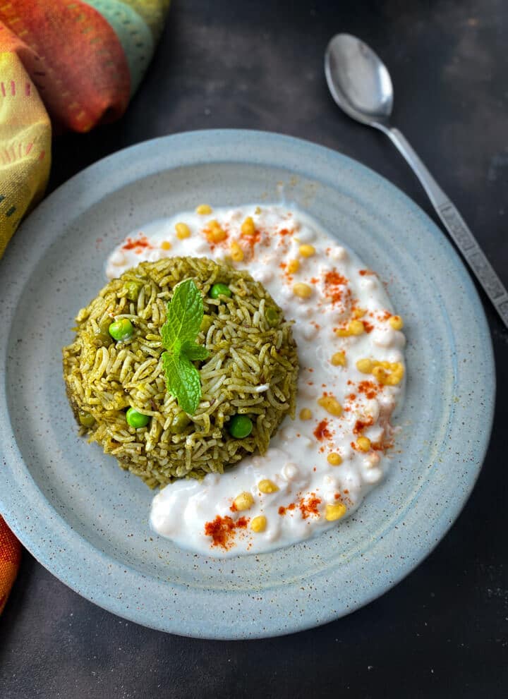 A light blue plate with a scoop of palak rice next to fresh raita.